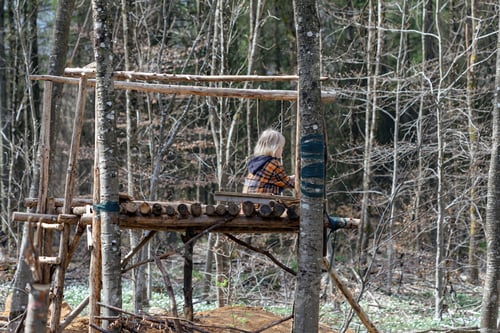 Preview: A blonde child is playing in the forest in a fort built by scouts