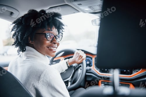 Preview: Looks back. Young african american woman sits inside of new modern car