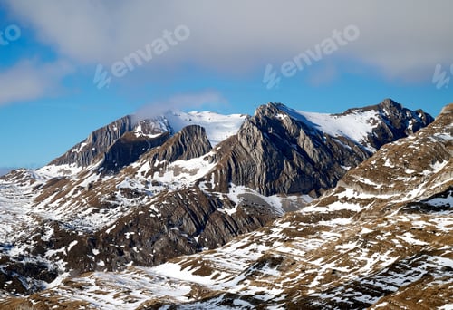 Preview: Stunning view of snow-capped mountains under a clear blue sky with scattered clouds