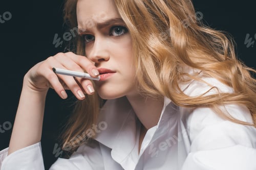 Preview: Portrait of young adult woman smoking a cigarette on black background, studio shot