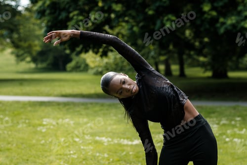 Preview: Portrait of black female athlete stretching in a park.