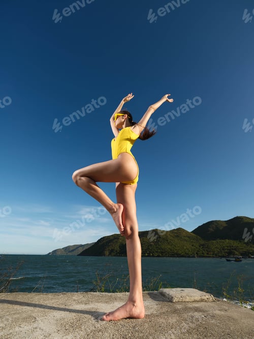 Preview: Woman handstand in yellow swimsuit on concrete wall, near water, with mountain background perfectly