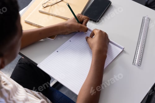 Preview: Writing in notebook, student focusing on schoolwork at desk with smartphone nearby