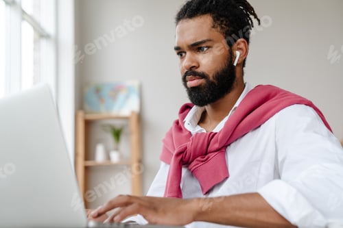 Preview: Serious african american guy in earphones working with laptop