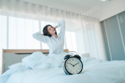 Preview: Young woman at home in morning, focus on alarm clock.