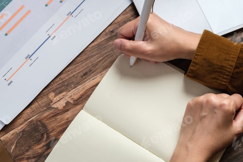 Preview: close uop woman hand writing on notebook at worknig desk at home