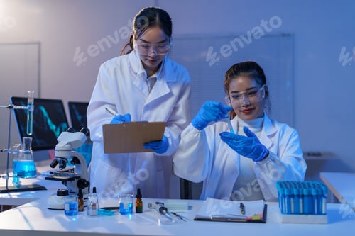 Preview: Two female scientists wearing lab coats, safety glasses, and gloves are conducting medical research