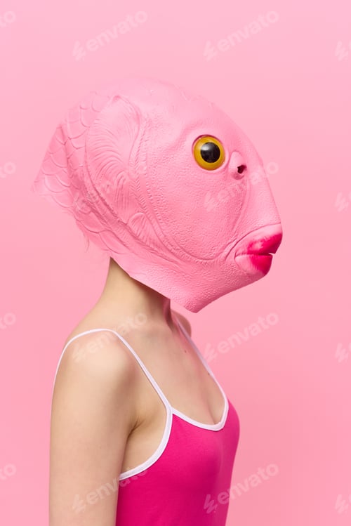 Preview: A woman in a pink fish head mask stands in profile against a pink background and looks into the