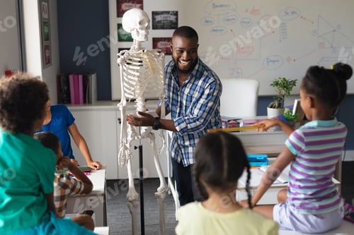 Preview: Happy african american young male teacher explaining skeleton to multiracial elementary students