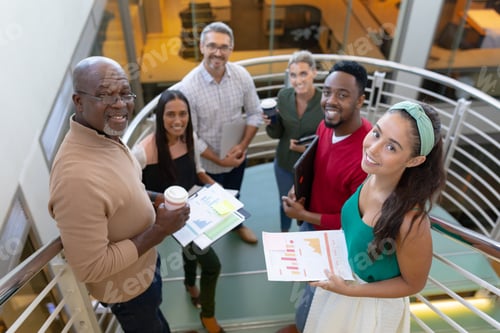 Preview: High angle portrait of smiling multiracial male and female advisors standing at staircase in office