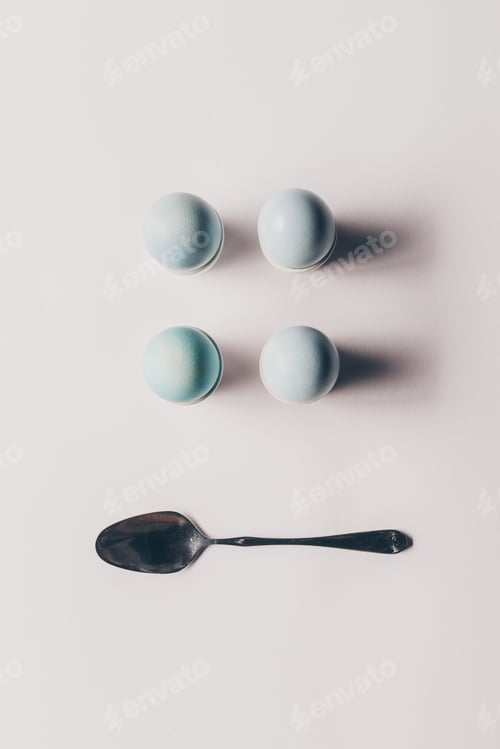 Preview: top view of four easter eggs on stands and spoon on white surface
