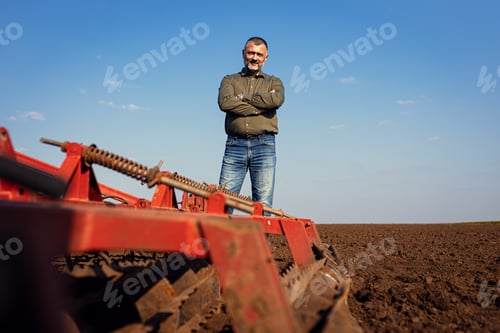 Preview: Portrait of satisfied farmer standing in field preparing to cultivate the land with a tractor.