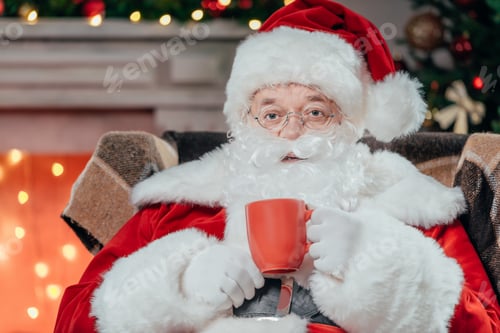 Preview: bearded santa claus in traditional red costume sitting in armchair and drinking coffee