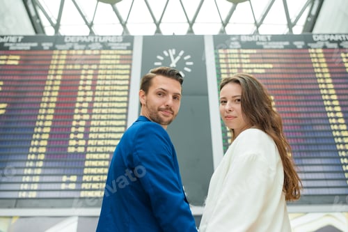 Preview: Young couple in international airport looking at the flight information board