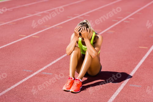 Preview: Upset female athlete sitting on running track
