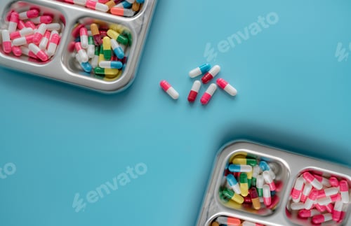 Preview: High angle view of multi-colored antibiotic capsule pills on stainless steel tray and blue