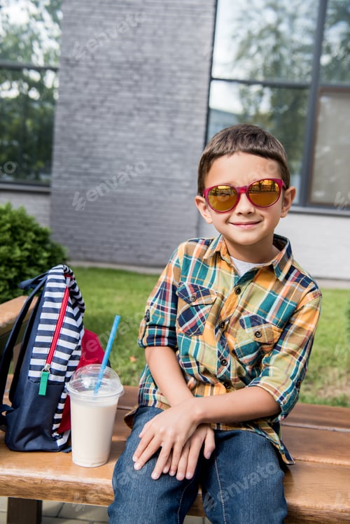 Preview: preschooler boy in sunglasses sitting on bench with backpack and milkshake