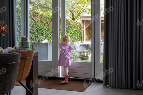 Preview: A young girl in a pink dress and red boots stands at an open door, looking out into a garden.