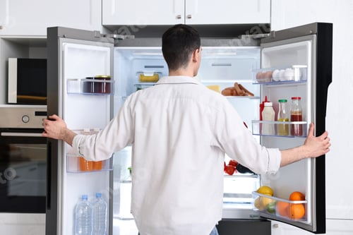 Preview: Man near refrigerator in kitchen at home, back view