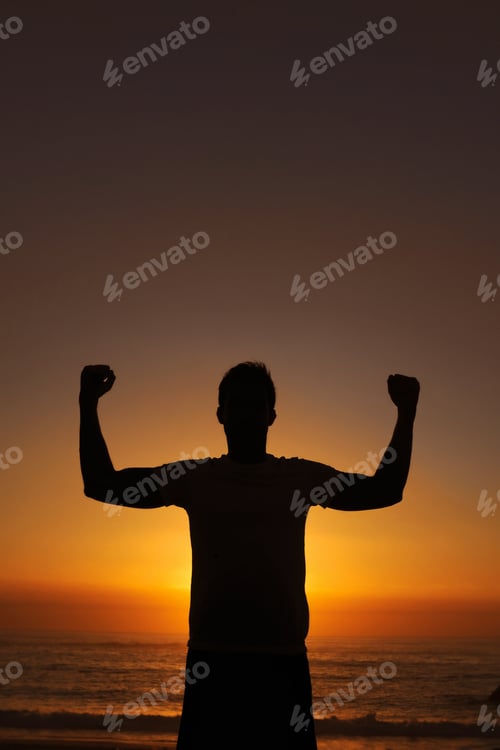 Preview: Silhouette of a man standing with his arms victoriously raised against the sunset