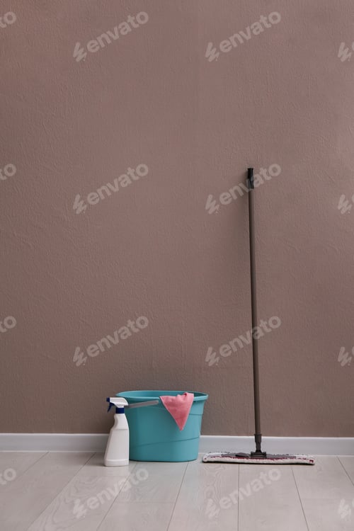 Preview: Floor mop, cleaning detergent and bucket with rag near brown wall indoors