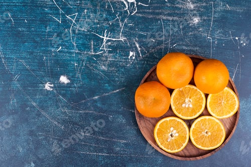Preview: Sliced oranges and mandarines on a wooden platter on blue background