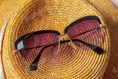 Preview: Stylish sunglasses placed on a straw hat during a sunny afternoon at the beach
