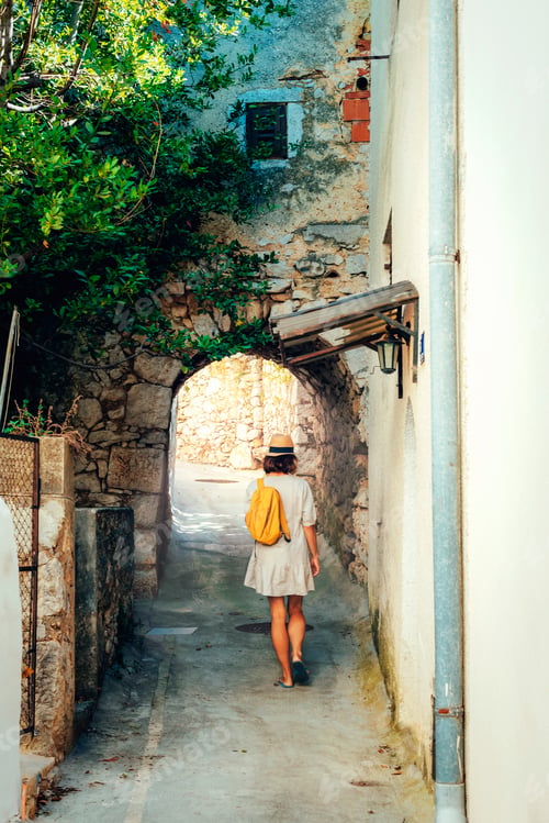 Preview: Girl tourist walking through ancient narrow street on a beautiful summer day in Omisalj town