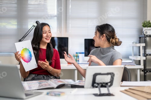 Preview: Pretty asian woman showing color palette to coworker aside working material on table in the office.