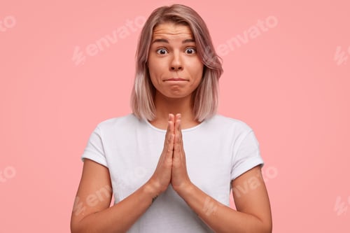 Preview: Attractive female model with bobbed hairstyle, keeps palms pressed together, looks hopefully at you,