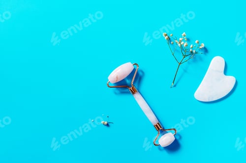 Preview: Rose quartz facial massage roller over blue background.