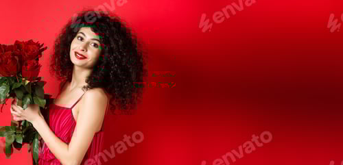 Preview: Happy beautiful woman in dress, holding flowers and smiling romantic, standing against red