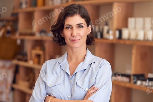 Portrait Of Female Owner Of Gift Store Standing In Front Of Shelves With Cosmetics And Candles
