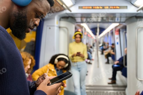 Preview: Young black man using smartphone and wearing headphones on subway train