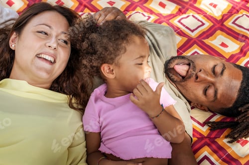 Preview: Happy multicultural family playing together on colorful picnic blanket outdoors
