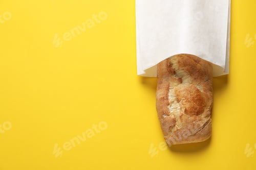 Preview: Paper bag with fresh baguette on yellow background, top view. Space for text