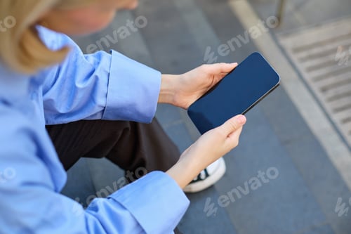 Preview: Shot from behind, young woman sitting on stairs on street, holding mobile phone in both hands