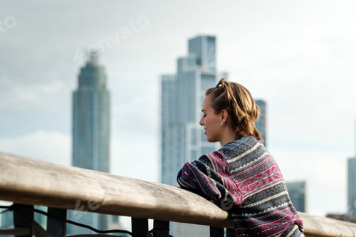 Preview: Young woman leaning on railing and contemplating city skyline