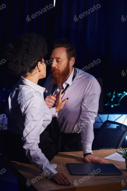 Preview: charismatic bearded businessman undressing near young african american woman in office at night