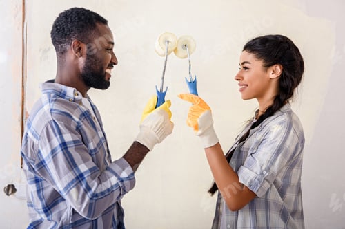 Preview: side view of couple with rolling brushes looking at each other while making renovation of home