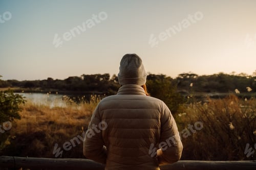 Preview: Person seated on a wooden fence gazing at water.