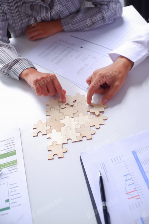 Preview: Closeup hands of two business people helping each other connecting jigsaw puzzle.