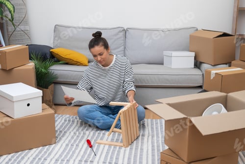 Preview: Woman tenant sits on the floor, assembling shelf amidst moving carton boxes rental space