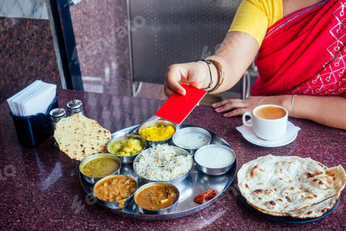 Preview: beautiful brunette woman in red sari paying by plastic card for traditional thali