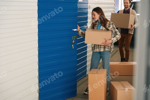 Preview: Woman and man with big cardboard boxes into warehouse with self storage unit