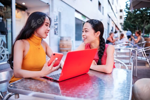 Preview: two asian women using a computer outdoor
