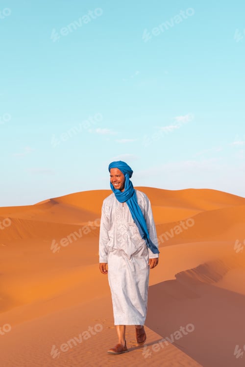 Preview: Smiling Berber male nomad in traditional clothing walking in the sahara desert at sunset