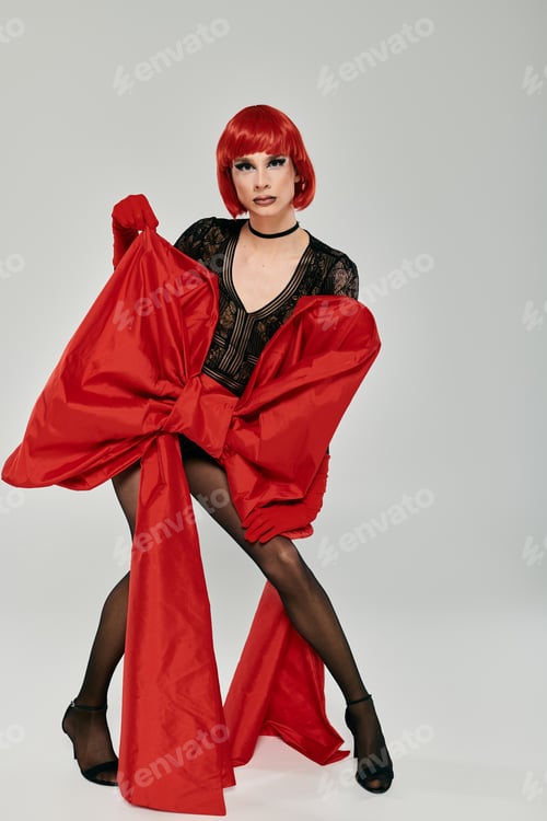 Preview: Stunning Young Drag Queen in Bold Red Ensemble Posing in Artistic Studio Setting