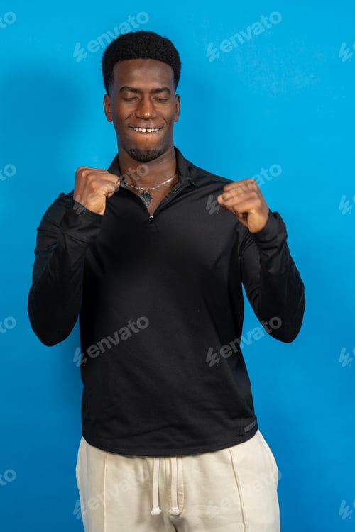 Preview: Young man dancing with closed eyes and fists raised on blue background