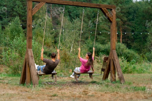 Preview: Loving couple man and girl riding on a large wooden swing overlooking a beautiful lake in nature